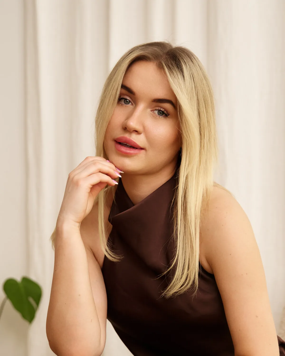 Karolina Fajer — portret na tle kremowej zasłony, z dłonią opartą o brodę