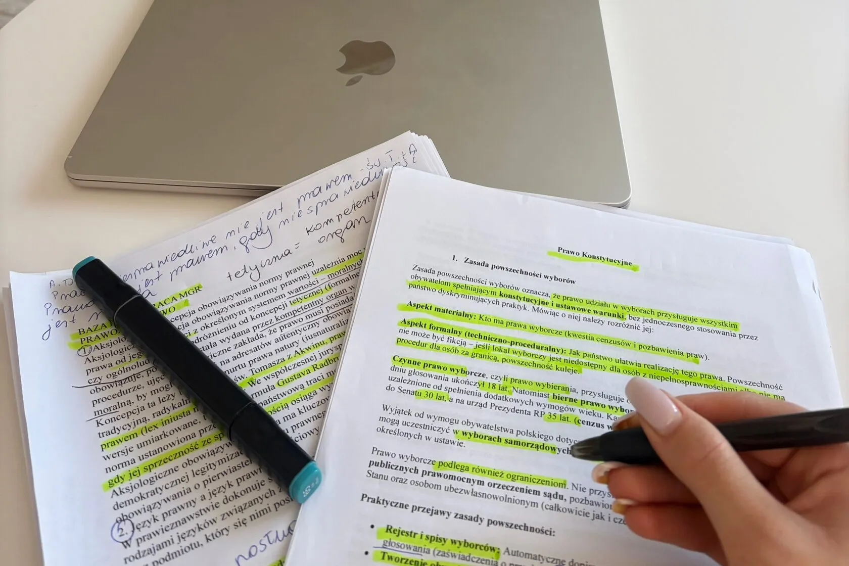 Wydrukowany materiał z prawa konstytucyjnego, zakreślony i opisany odręcznie na marginesie, obok kartek z notatkami i zamkniętego laptopa